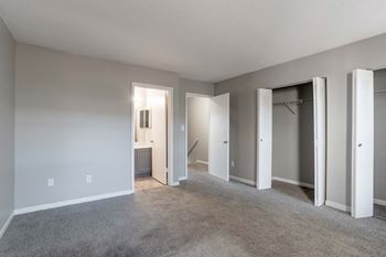 A spacious room with a carpeted floor and white walls, featuring a row of white doors.
